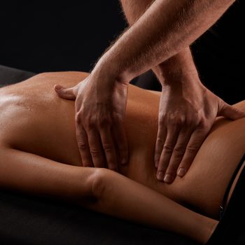 Über uns 17 handsome male masseur giving massage to girl on black background, concept of therapeutic relaxing massage
